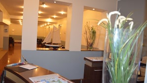 A reception desk with a map, a sailboat model, and a plant in a vase. - Hotel Mercedes Hamburg (Hamburg)