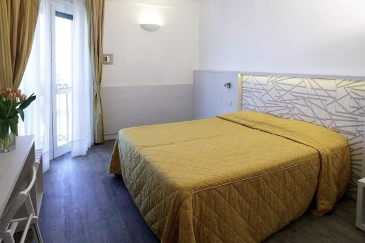 A hotel room with a bed, a desk, a chair, and a vase of flowers.