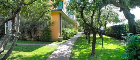 A pathway leading to a building with a balcony, surrounded by greenery and trees.