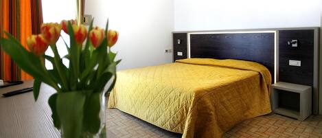 Una habitación de hotel con una cama, una mesita de noche y un jarrón de tulipanes.