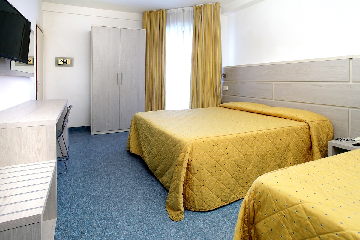 A hotel room with two beds, a desk, a wardrobe, and a television.