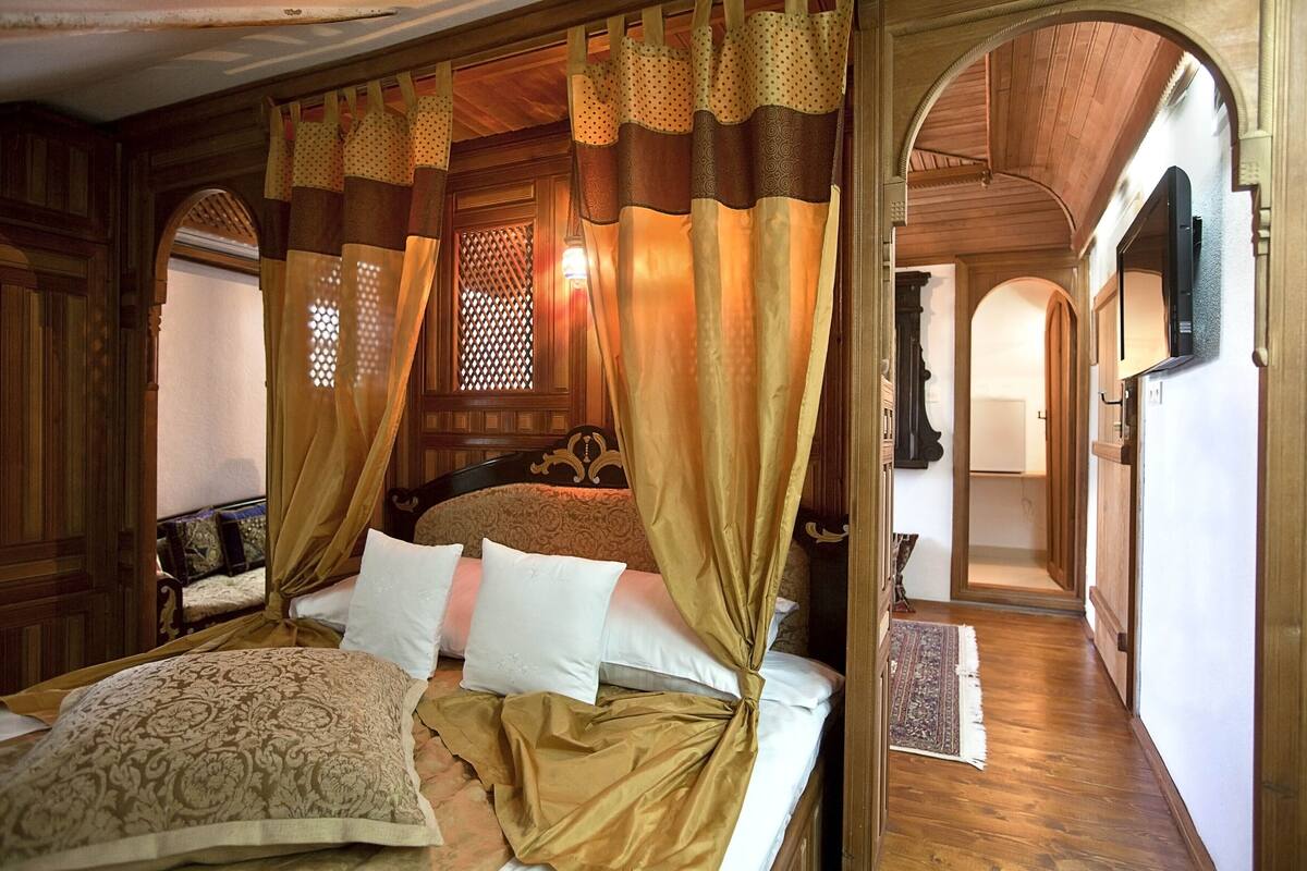 Une pièce avec un lit, des murs en bois et une fenêtre ornée d’un motif en treillis.