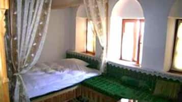 Quarto com cama, sofá verde, janela e espelho.