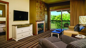 Habitación de hotel con chimenea de piedra, televisión, sofá y balcón con vistas a la vegetación.