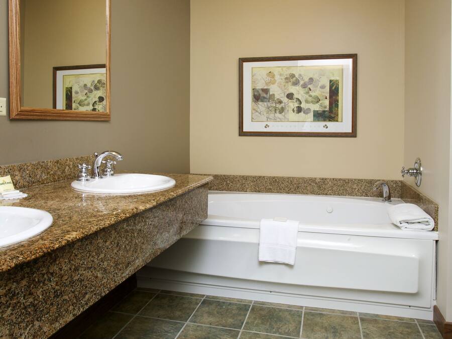 A bathroom with two sinks, a large mirror, a framed artwork, and a bathtub.