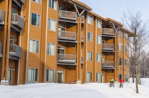 Un edificio de madera de varios pisos con balcones, suelo cubierto de nieve y cielo despejado.