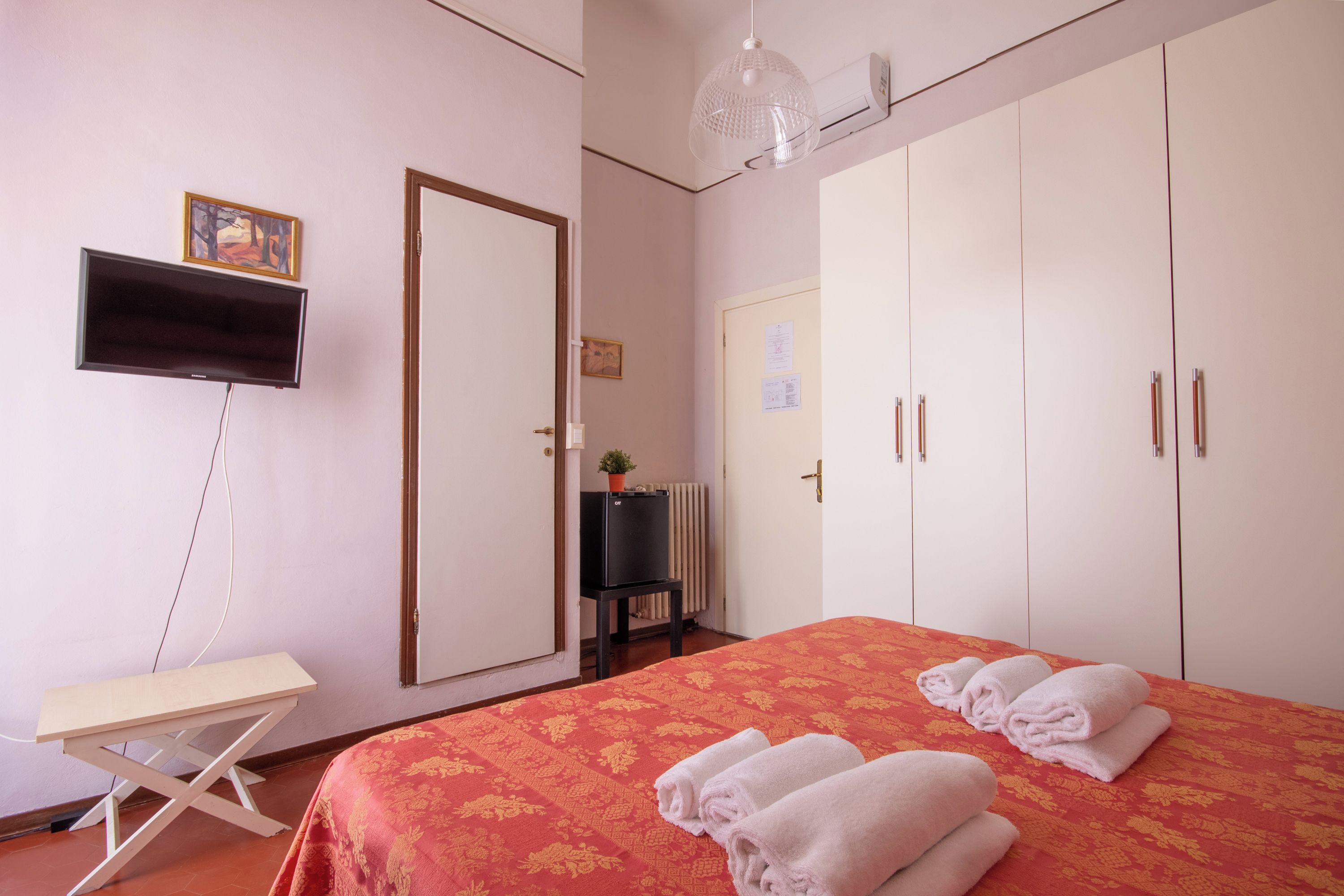Ein Hotelzimmer mit Bett, Schreibtisch, Fernseher, Kleiderschrank und Heizkörper.