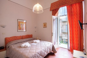 Un dormitorio con cama, mesita de noche, lámpara colgante, un cuadro en la pared y una ventana con cortinas.