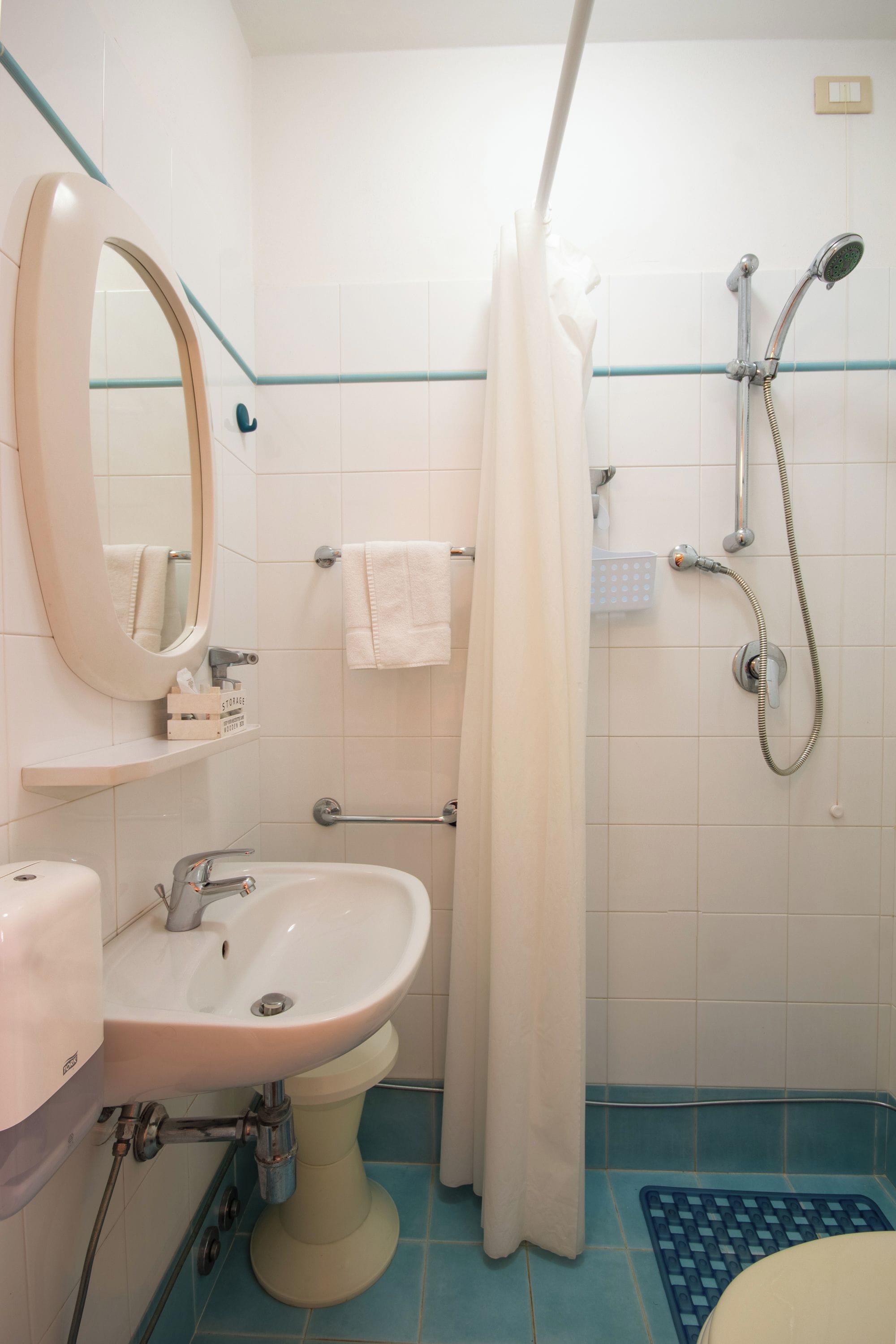 Un baño con lavamanos, espejo, ducha y toallero.
