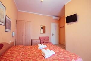 Habitación de hotel con cama, armario, escritorio, silla, televisor y aire acondicionado.