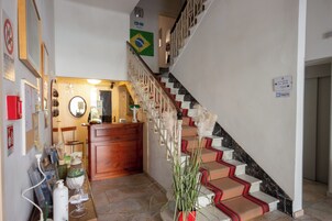 Un vestíbulo de hotel con mostrador de recepción, una escalera con escalones rojos y blancos, y una bandera de Brasil en la pared.