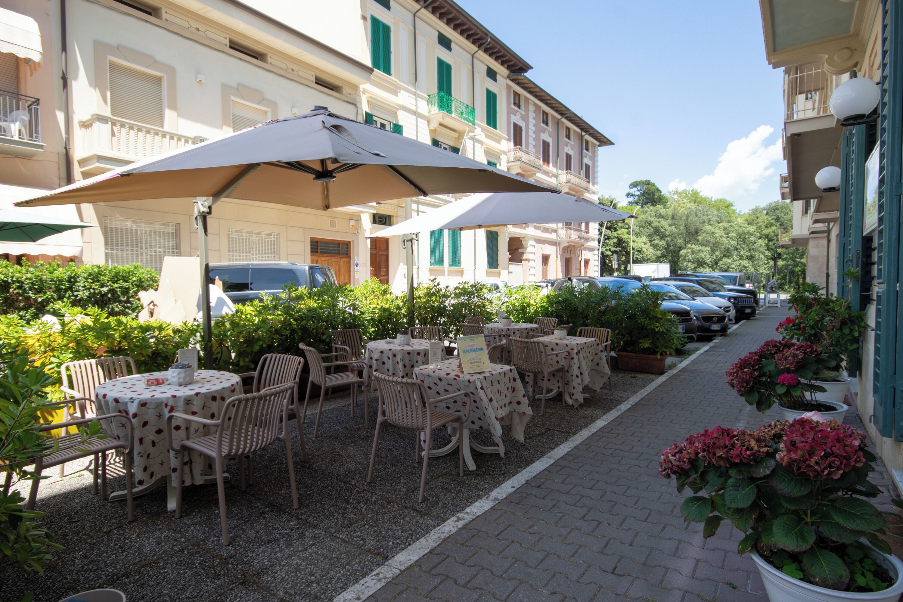 An outdoor cafe with tables and chairs, umbrellas, and potted plants.