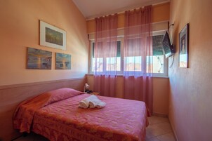 A hotel room with a bed, a nightstand, a window with curtains, and wall art.
