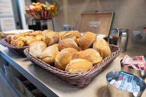 A buffet table with baskets of bread and pastries, a fruit bowl, and a sign indicating a bakery section. - Nemea Appart Hotel Toulouse Aéroport (Toulouse)