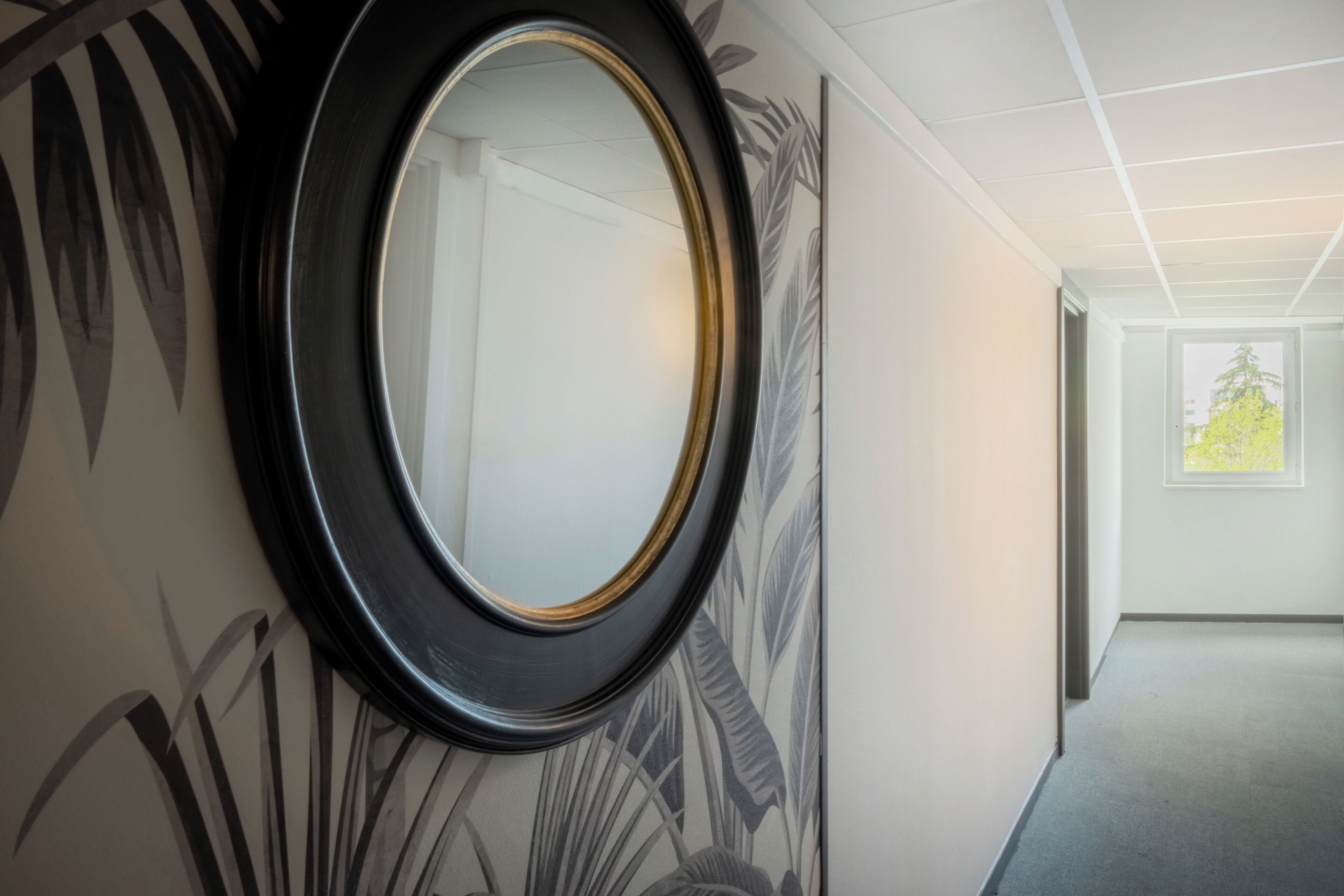 Een hal met een grote spiegel, een behang met patroon en een deur naar een andere kamer.