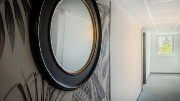 A hallway with a large mirror, a patterned wall, and a door leading to another room.