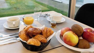Taula de l'esmorzar amb croissants, pomes, kiwi, suc d'aranja i cafè.