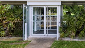 A reception area with glass doors, a concrete pathway, and surrounding greenery. - Nemea Appart Hotel Toulouse Aéroport (Toulouse)