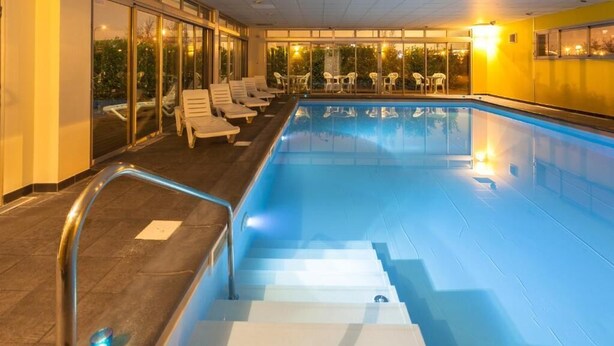An indoor swimming pool with steps leading into it, surrounded by lounge chairs and tables. - Nemea Appart Hotel Toulouse Aéroport (Toulouse)