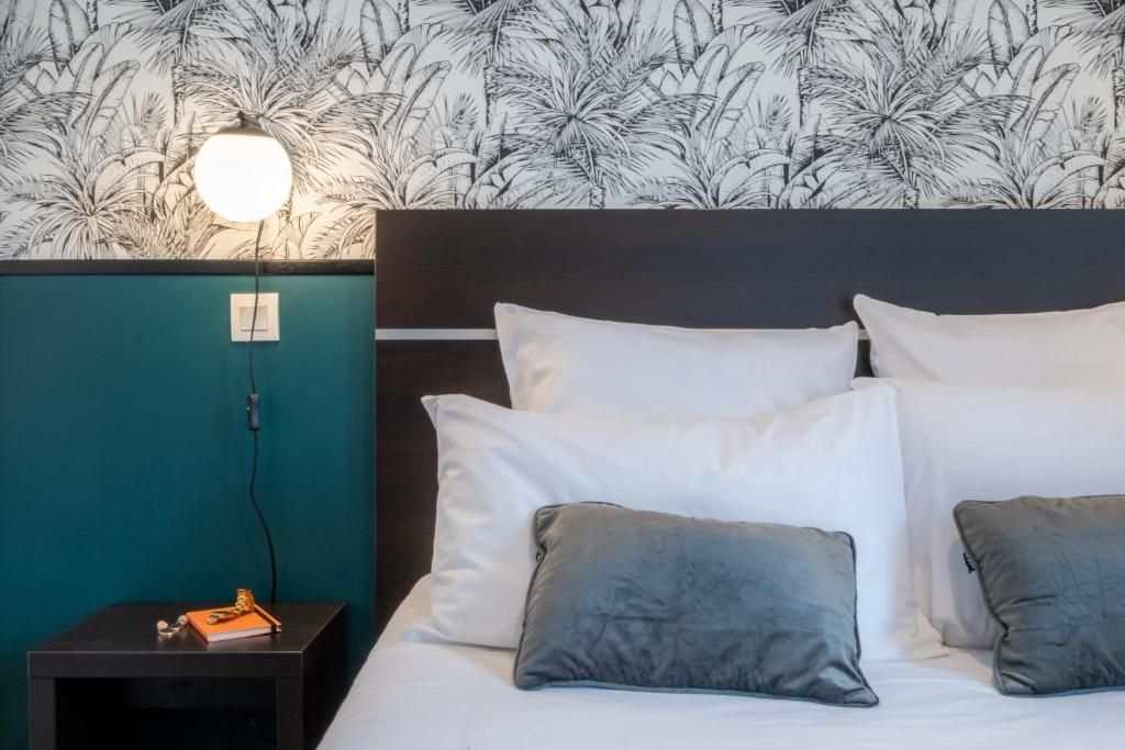 A neatly made bed with white and gray pillows, a teal accent wall, and a wall-mounted lamp.