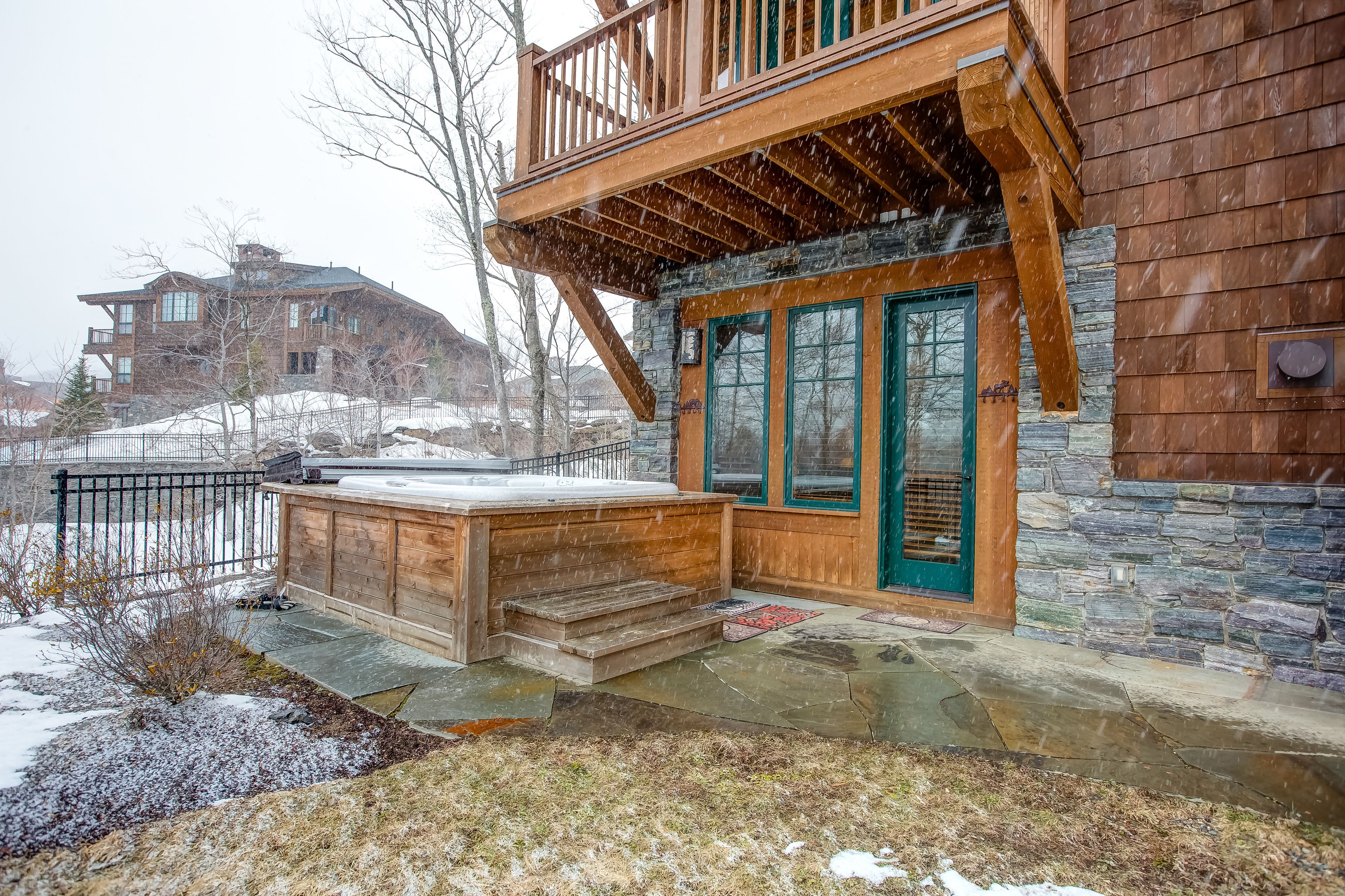 A wooden house with a stone foundation, a balcony, and a hot tub.