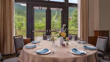 Mesa de comedor lista para seis personas con vista a una montaña boscosa.