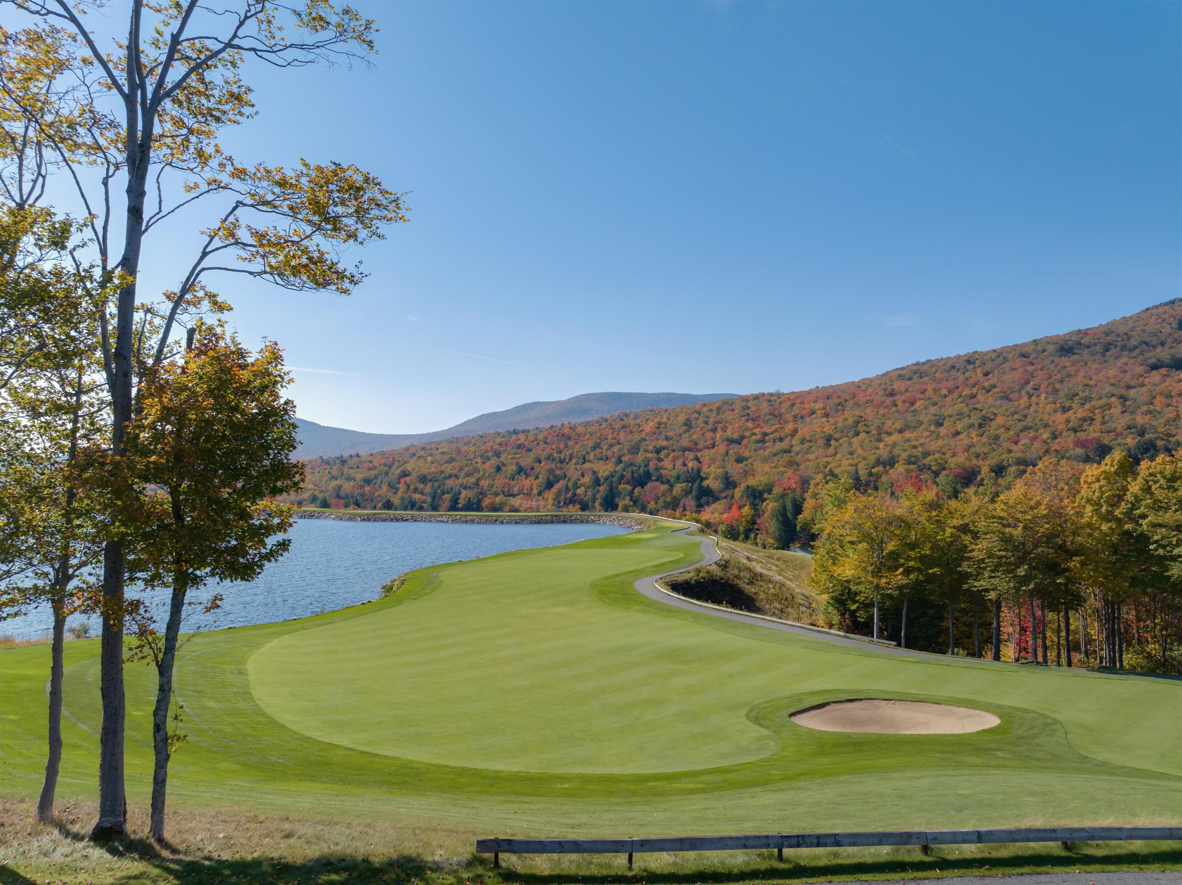 A golf course with a lake, trees, and hills in the background.