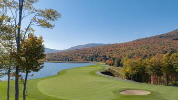 A golf course with a lake, trees, and hills in the background.