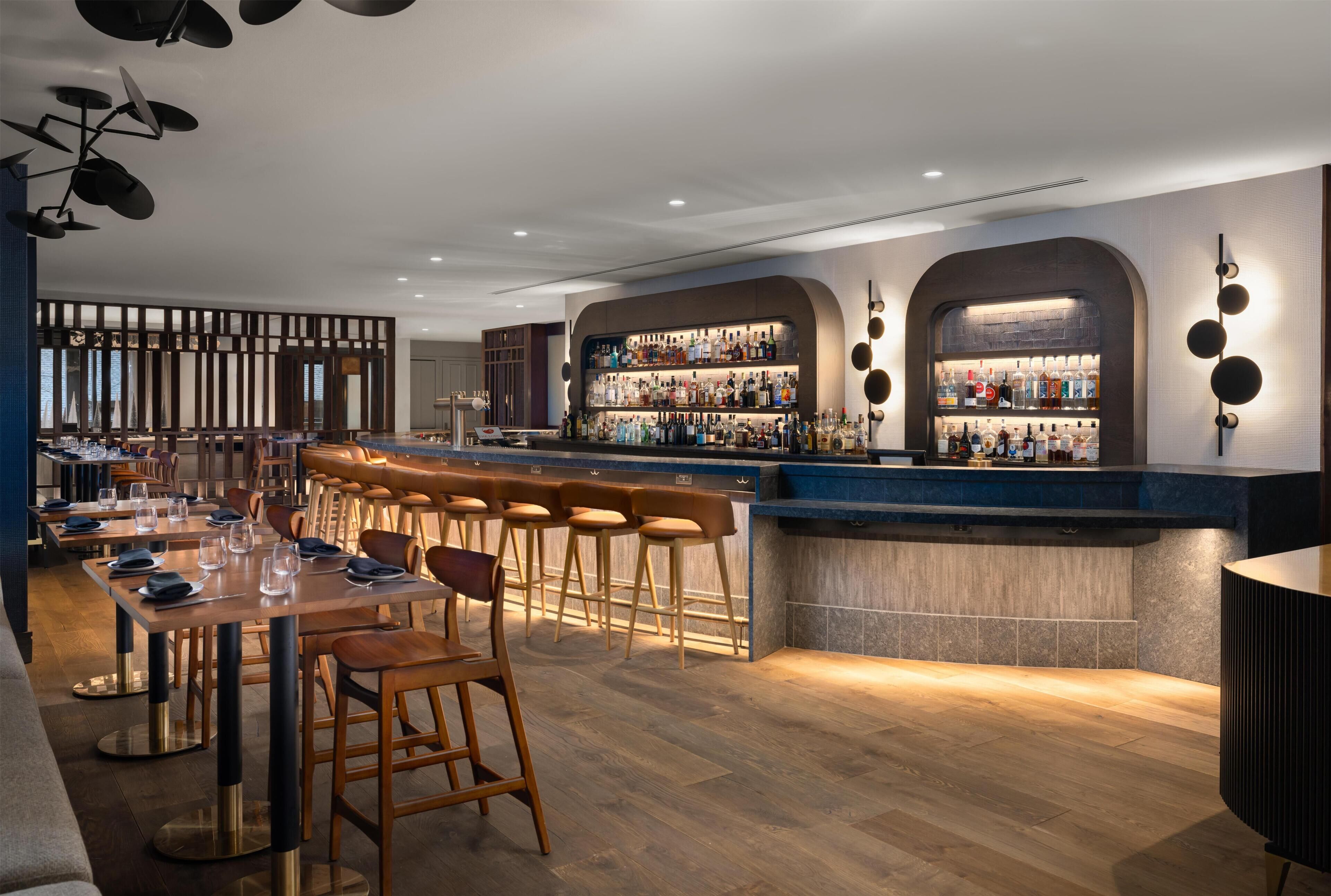 A modern bar area with stools, a counter, and a variety of bottles.