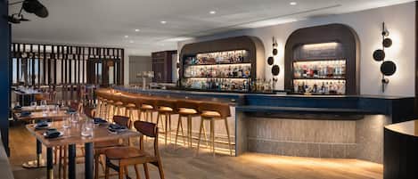 A modern bar area with stools, a counter, and a variety of bottles.