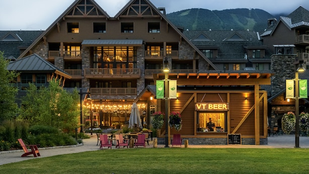 A lodge with a prominent 'Vt Beer' sign, outdoor seating, and a mountainous backdrop. - The Lodge at Spruce Peak, a Destination by Hyatt Residence (Stowe)