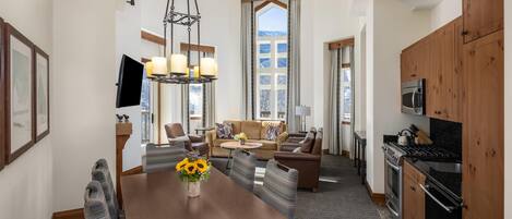 Une chambre d’hôtel moderne dotée d’un coin repas, d’un ensemble de canapés, d’une cuisine et d’une grande fenêtre offrant une vue panoramique.