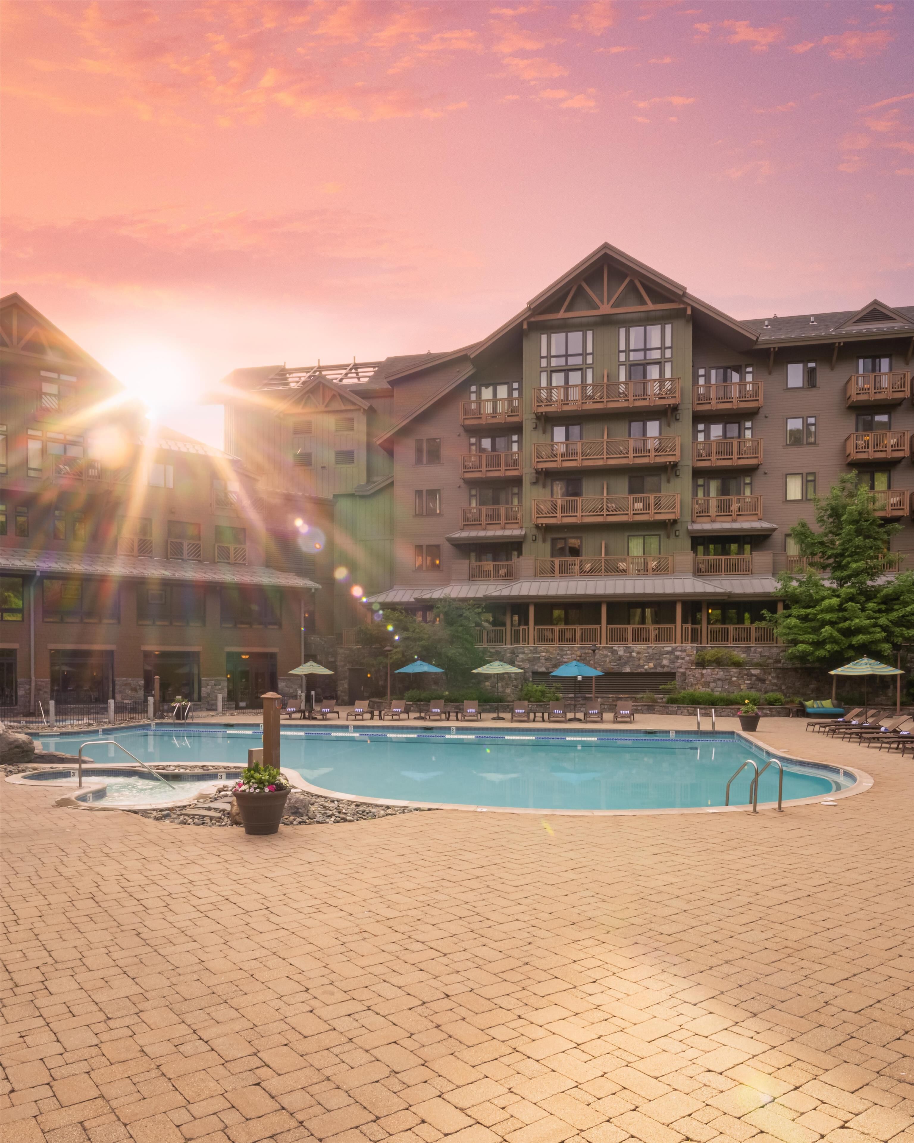 A hotel with a swimming pool, outdoor seating, and a sunset view.