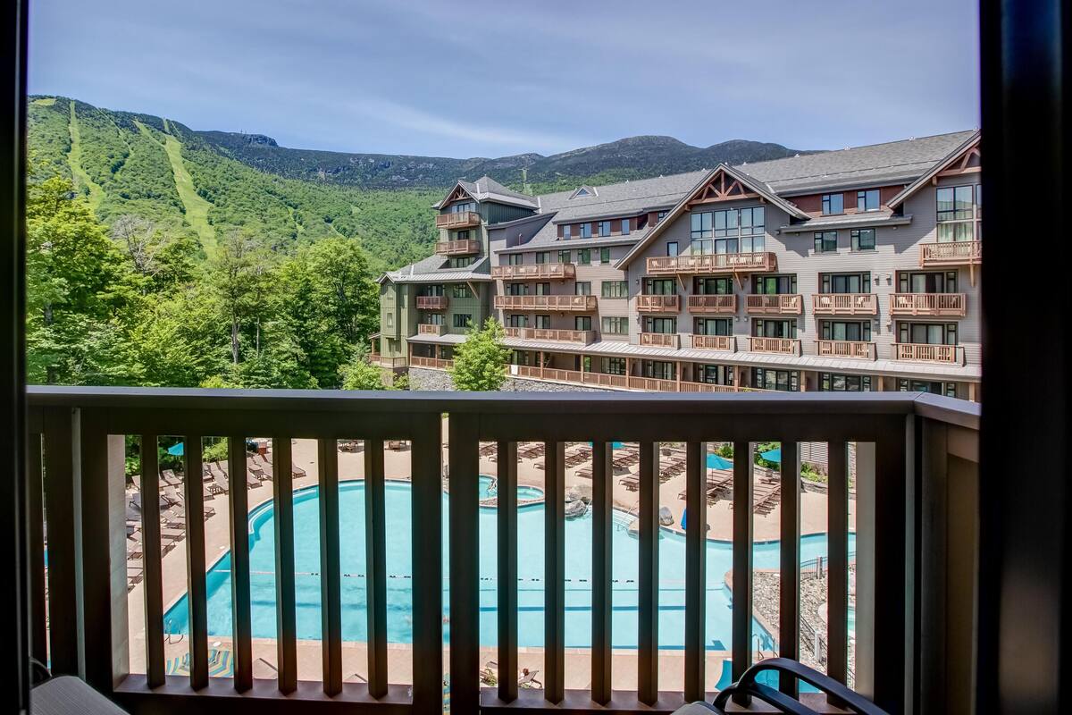 A hotel with a pool, multiple balconies, and a mountainous backdrop.