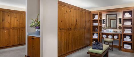 A walk-in closet with wooden lockers, a bench, a mirror, and shelves with folded towels.