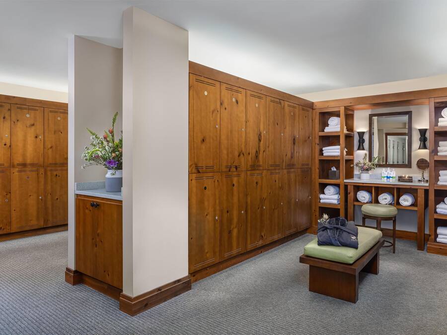A walk-in closet with wooden lockers, a bench, a mirror, and shelves with folded towels.
