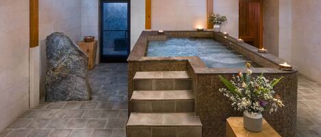 Un área de spa con un jacuzzi, escalones de piedra y un banco de madera con un florero.