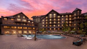 A multi-story hotel with a swimming pool and outdoor seating area. - The Lodge at Spruce Peak, a Destination by Hyatt Residence (Stowe)