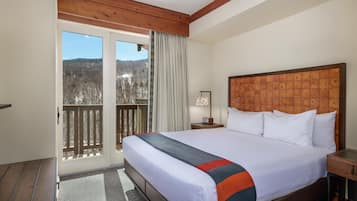 Habitación de hotel con una cama grande, cabecera de madera, una mesita de noche, una lámpara y vistas a un balcón con barandilla de madera.