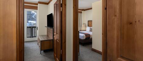 A hallway with wooden doors leading to a bedroom with a bed and a TV.