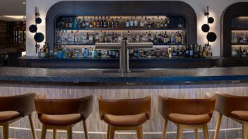 A bar area with a counter, multiple shelves of bottles, and three bar stools.