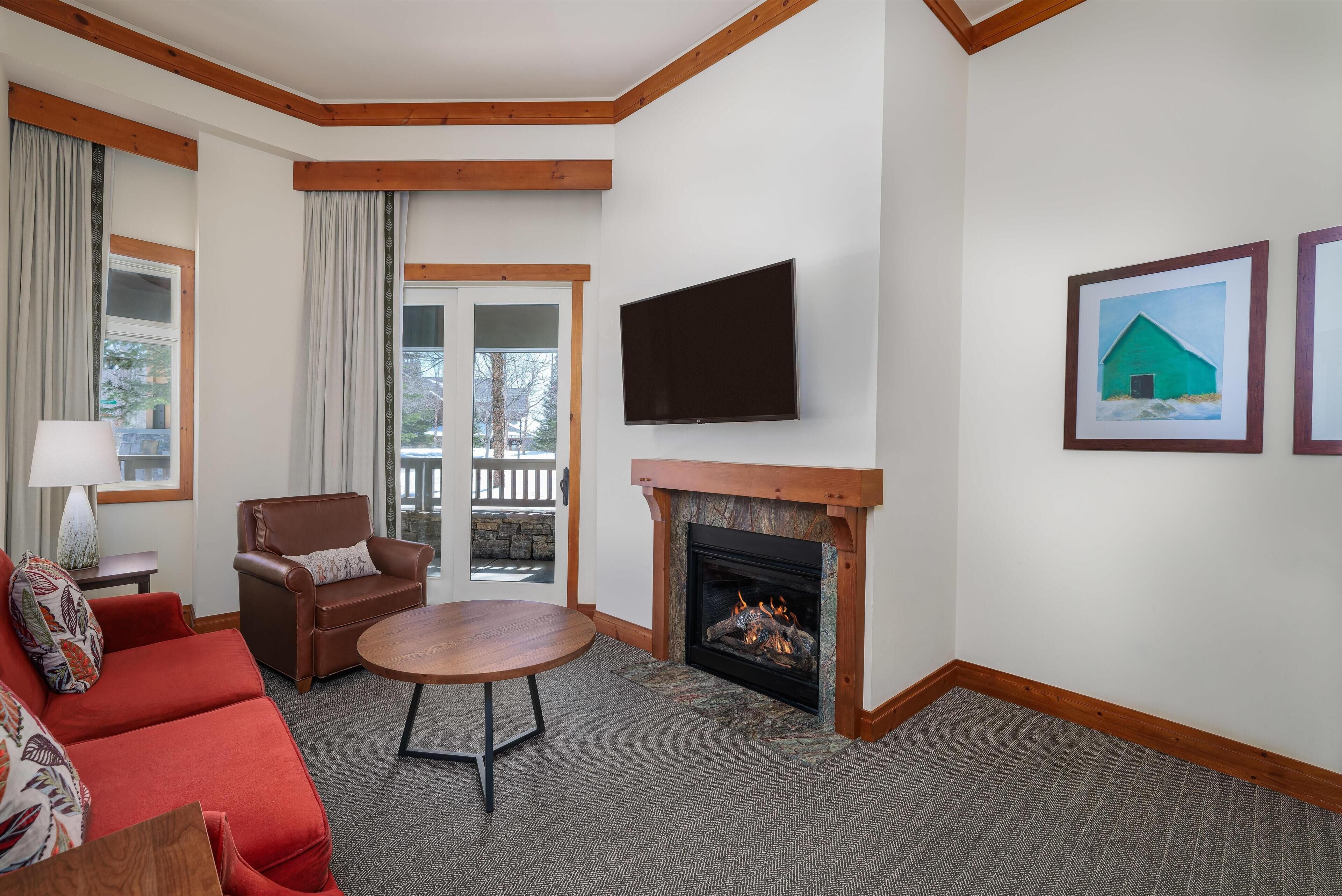 A living room with a fireplace, a flat-screen TV, a red sofa, a brown armchair, and a dining table.