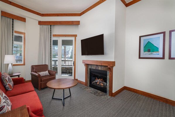A living room with a fireplace, a flat-screen TV, a red sofa, a brown armchair, and a dining table.