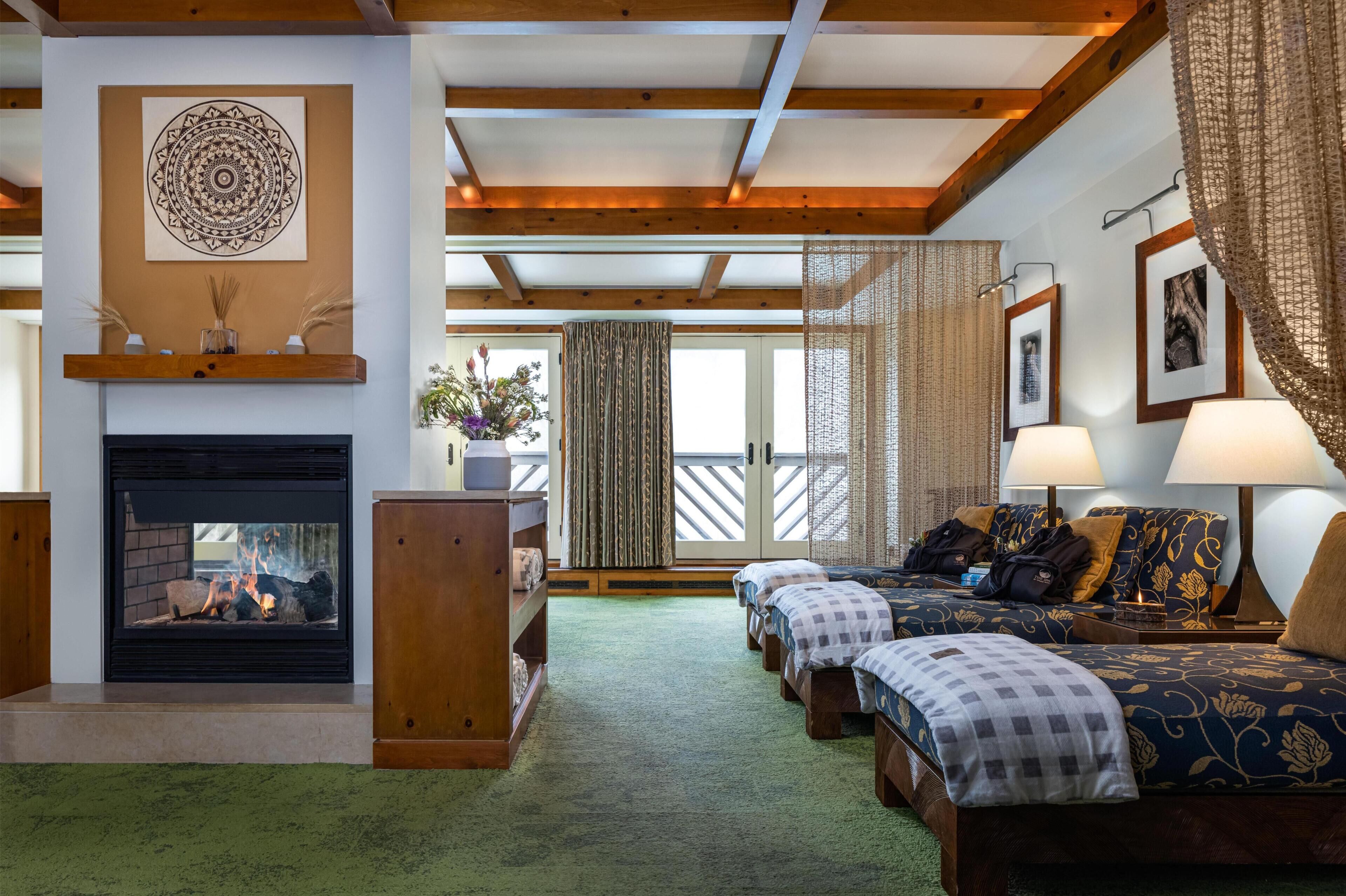 A room with a fireplace, two beds, a sofa, and a large window with curtains.