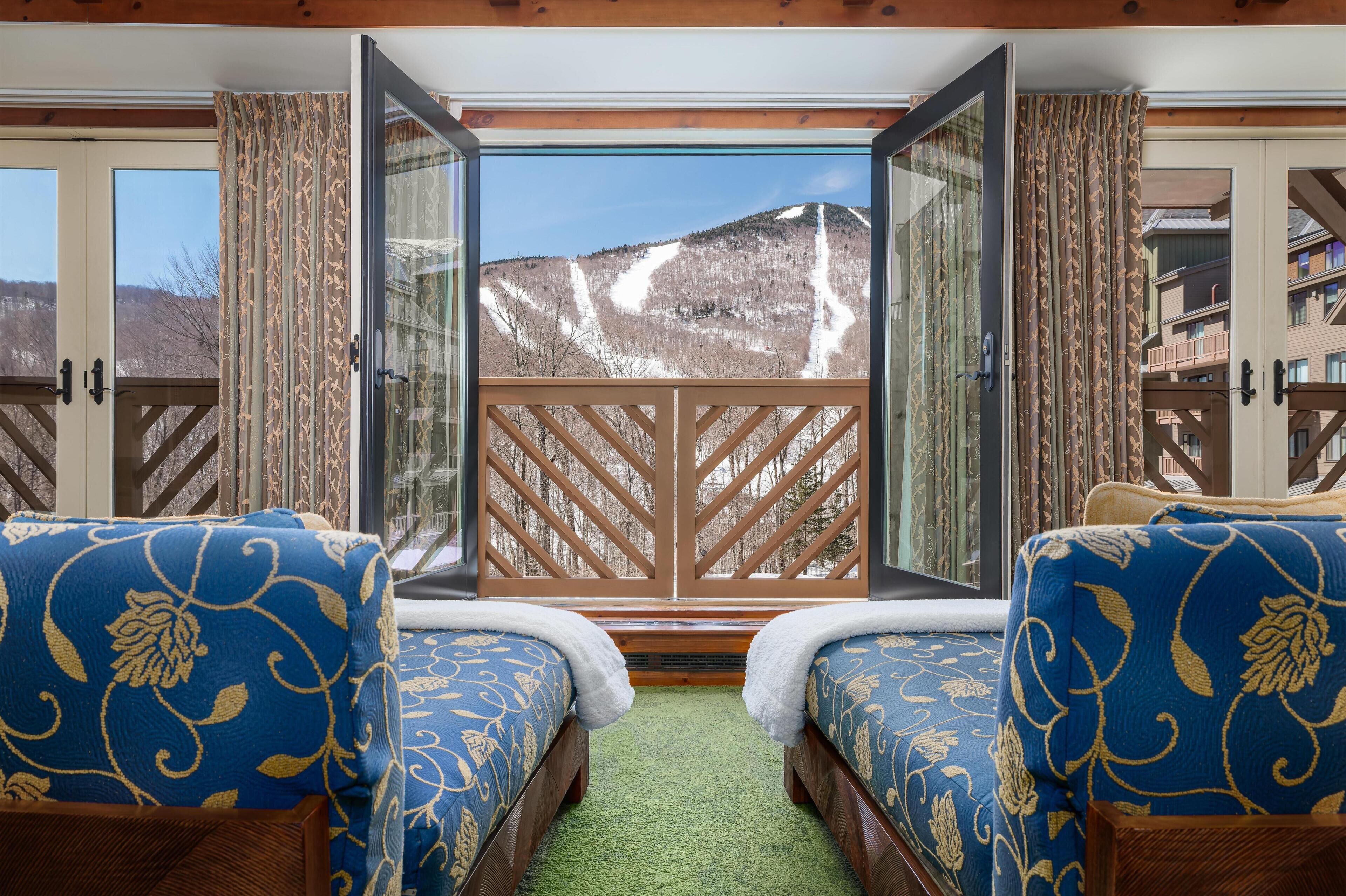 A room with two beds, a large window, and a view of a mountain.