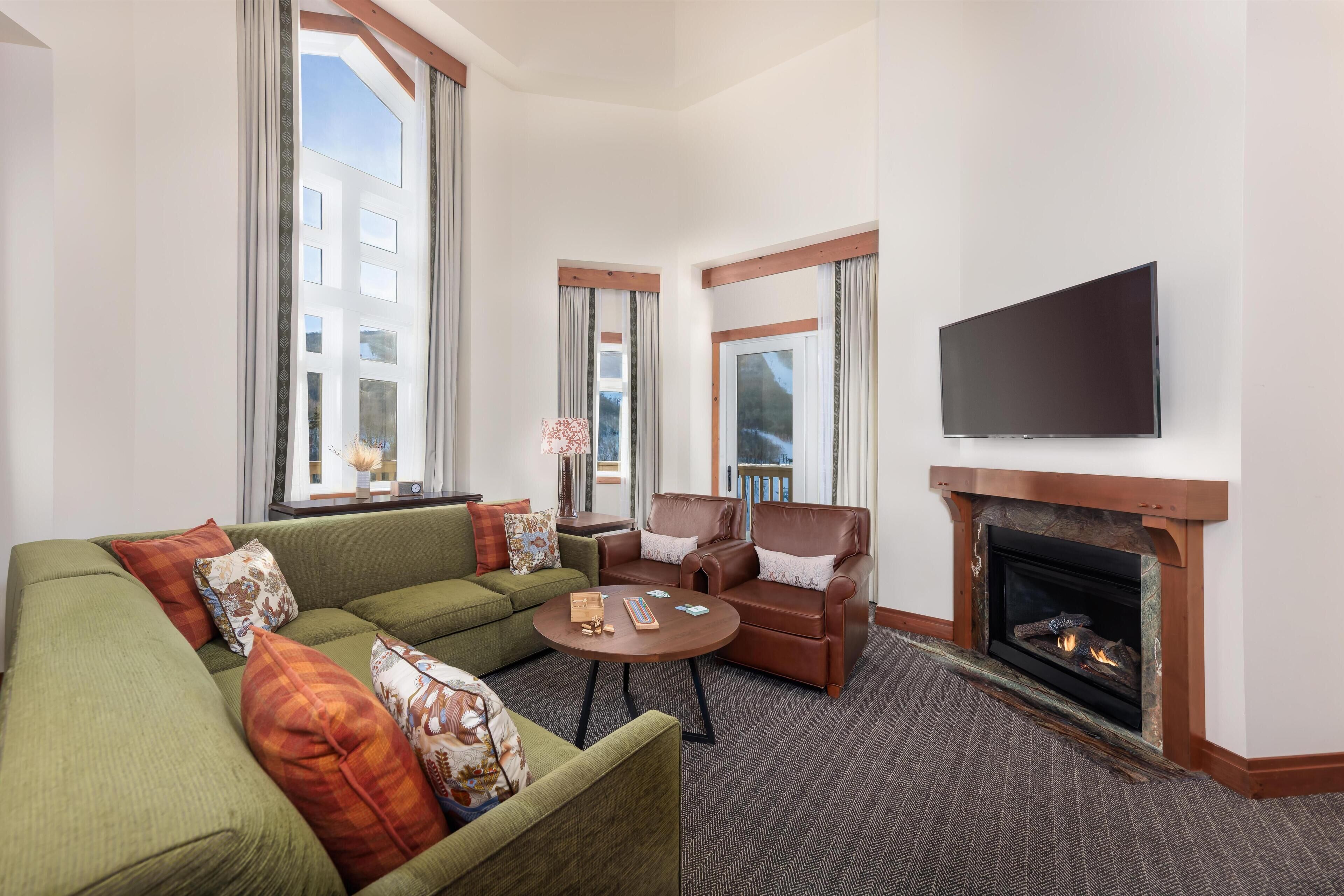 A living room with a fireplace, a flat-screen TV, and large windows.