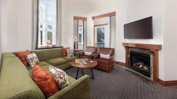 A living room with a fireplace, a flat-screen TV, and large windows.