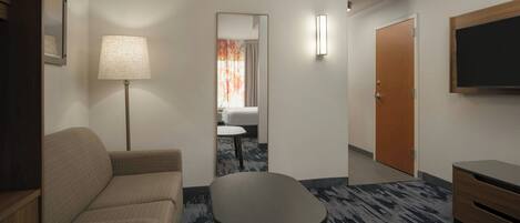 A hotel room with a sofa, a small table, a lamp, a mirror, a door, and a TV.