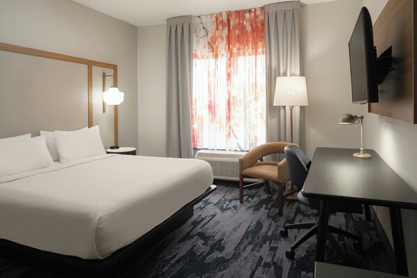 A hotel room with a large bed, a desk, a chair, a TV, and a window with curtains.