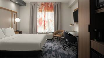A hotel room with a large bed, a desk, a chair, a television, and a window with curtains.